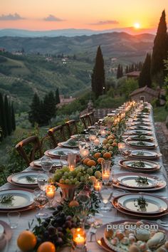 a long table is set with plates and candles in front of the sun setting over an italian countryside