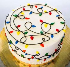 a white cake with multicolored icing and lights on it sitting on a gold plate