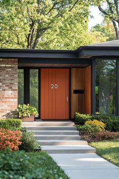 the front entrance to a modern home with an orange door and brick walkway leading up to it