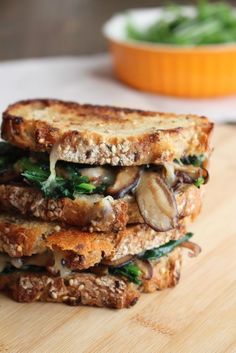 two sandwiches stacked on top of each other with mushrooms and spinach in the background