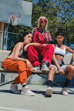 three young women sitting on a bench in front of a basketball hoop, one wearing sunglasses