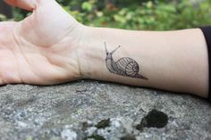 a small snail tattoo on the left wrist and right hand is shown in black ink