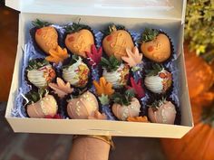 a hand is holding a box of chocolate covered strawberries with decorations on them and pumpkins in the background