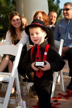 a young boy in a top hat and tie walking down the aisle at a wedding