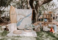 an outdoor area with surfboards, baskets and other items on the grass next to a tree