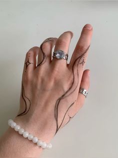 a woman's hand with tattoos on it holding onto a white beaded bracelet