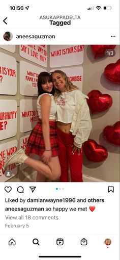 two women standing next to each other in front of a wall with red hearts on it