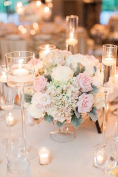 the table is set with wine glasses, candles and flower centerpieces on it