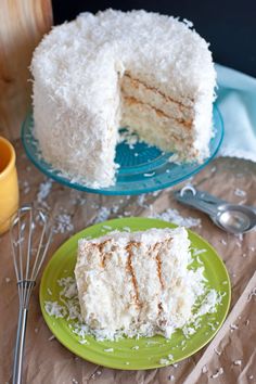 a piece of coconut cake on a green plate next to a fork and spoons