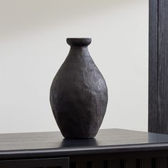 a black vase sitting on top of a wooden table next to a white wall in a room