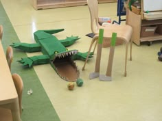 a toy alligator is laying on the floor next to a chair and table in a classroom