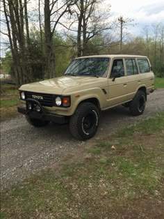 an suv parked on the side of a dirt road in front of trees and grass