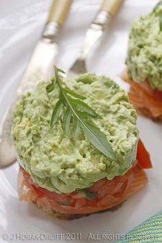 two small sandwiches are topped with guacamole and tomatoes