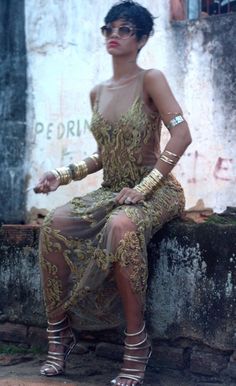 a woman sitting on top of a stone wall next to a brick building wearing high heels