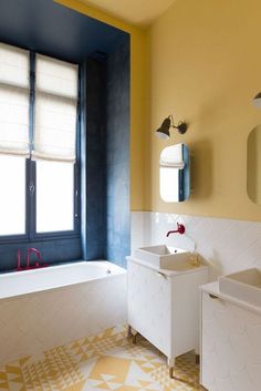 a bathroom with yellow and blue walls, white sink and bathtub next to window