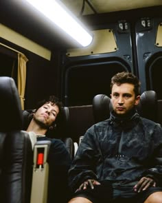 two men are sitting on a train looking at something in the distance with their eyes closed