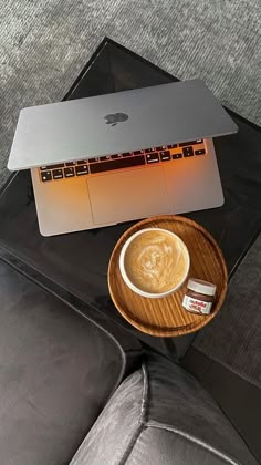 a cup of coffee sitting on top of a wooden plate next to a laptop computer