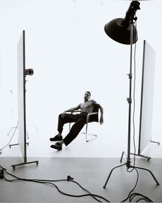 a man sitting in a chair next to two lights and a tripod on the floor