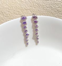 Amethyst Purple Earrings featuring semi precious purple stones and cz diamonds. Perfect for any special occasion look or a wedding bridesmaid look. These Purple Dangle Earrings surely add a touch of super luxury in your entire look. Also a perfect gift for her or gift for mom. *𝐏𝐑𝐎𝐃𝐔𝐂𝐓 𝐃𝐄𝐓𝐀𝐈𝐋* * 𝐌𝐚𝐭𝐞𝐫𝐢𝐚𝐥: Brass * 𝐏𝐥𝐚𝐭𝐢𝐧𝐠: White Rhodium Plated * 𝐒𝐭𝐨𝐧𝐞: AAA-quality CZ diamond. *𝐃𝐈𝐌𝐄𝐍𝐒𝐈𝐎𝐍𝐒* * 𝐖𝐞𝐢𝐠𝐡𝐭: 3 gm each * 𝐋𝐞𝐧𝐠𝐭𝐡: 5 cm * 𝐖𝐢𝐝𝐭𝐡:  1 cm Purple Drop Chandelier Earrings For Formal Occasions, Purple Gemstone Accented Dangle Earrings, Purple Gemstone Dangle Earrings, Purple Dangle Earrings With Gemstone Accents, Purple Crystal Jewelry With Matching Earrings, Elegant Purple Gemstone Chandelier Earrings, Purple Gemstone Accented Drop Earrings, Purple Sparkling Stone Drop Earrings, Purple Drop Earrings With Gemstone Accents