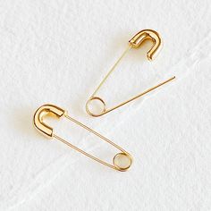 two pairs of gold - plated safety pins on white paper with clippings