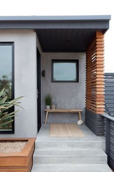 a modern house with wooden steps leading to the front door and patio area, along with potted plants