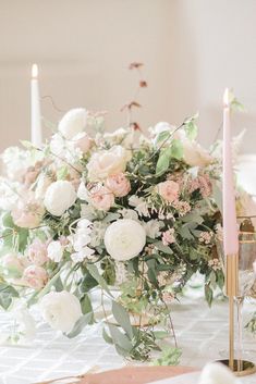 a vase filled with white and pink flowers on top of a table next to candles