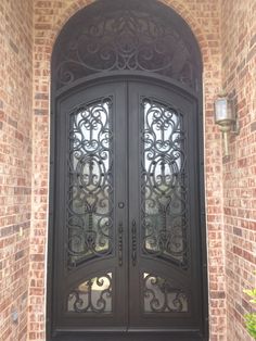 a black double door with intricate iron work on the front and side doors that lead into a brick building