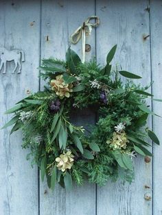 a wreath hanging on the side of a wooden building with flowers and leaves around it