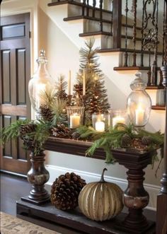 a mantle with pine cones, candles and evergreens on it in front of a staircase