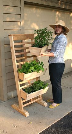 a woman standing next to a wooden planter filled with green plants in front of a garage