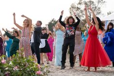 a group of people standing on top of a sandy beach holding hands up in the air