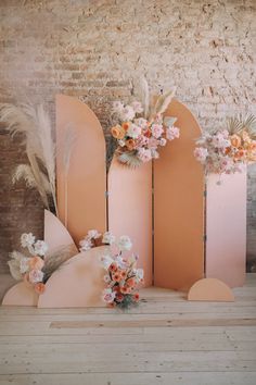 three pink vases with flowers and feathers in them sitting on a wooden floor next to a brick wall