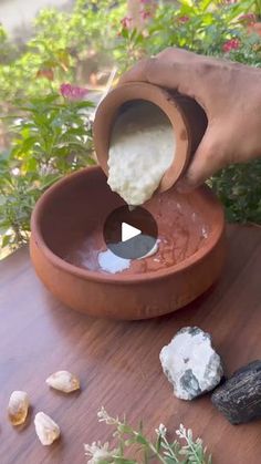 someone is pouring something into a bowl with rocks and plants in the backgroud