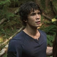 a young man holding a frisbee in his hand while standing in the woods