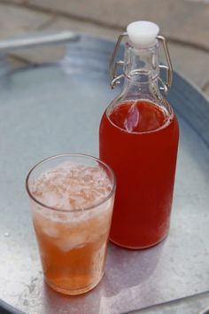 a bottle of liquid next to a glass on a metal tray with a drink in it