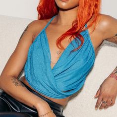 a woman with red hair sitting on a couch wearing a blue top and black leather pants