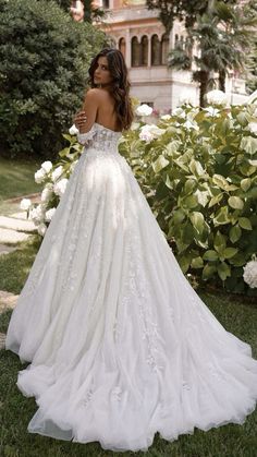 a woman in a white wedding dress standing on the grass with flowers behind her back