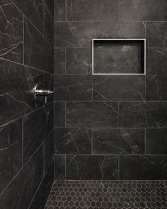 the shower is made up of black marble and has a metal grate in it