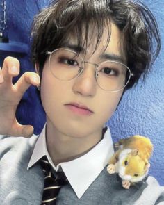 a young man wearing glasses and holding a small toy mouse in his right hand while standing against a blue wall