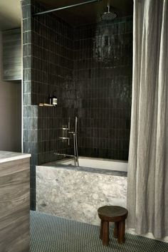 a black and white tiled bathroom with a stool next to the bathtub that is open