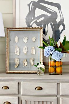 a vase with flowers sitting on top of a dresser next to a framed photograph and shells