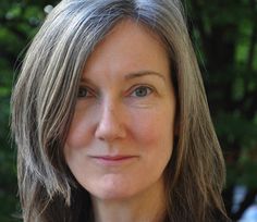 a woman with grey hair and blue eyes is looking at the camera while standing in front of some trees