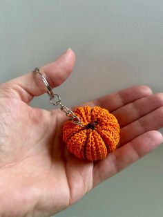 a small orange crochet pumpkin keychain in someone's left hand