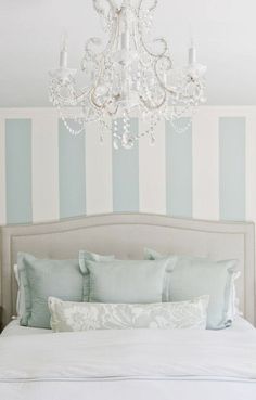 a chandelier hanging from the ceiling above a bed in a bedroom with blue and white striped walls