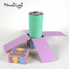 a can sitting on top of a purple and green box next to two blocks of paper