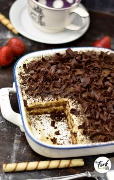 a cake in a pan with chocolate chips on top and strawberries next to it