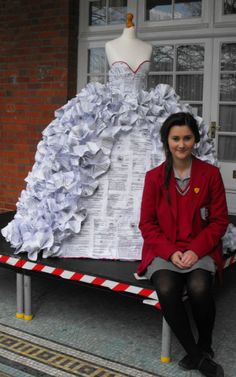 a woman sitting in front of a dress made out of newspaper