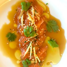 a white plate topped with fish covered in sauce and garnished with parsley