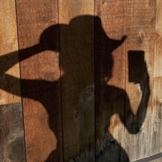 a shadow of a person holding a cell phone in front of a wooden wall with a sign on it