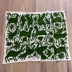 a green and white table cloth with various animals in the forest on it, sitting on a wooden floor